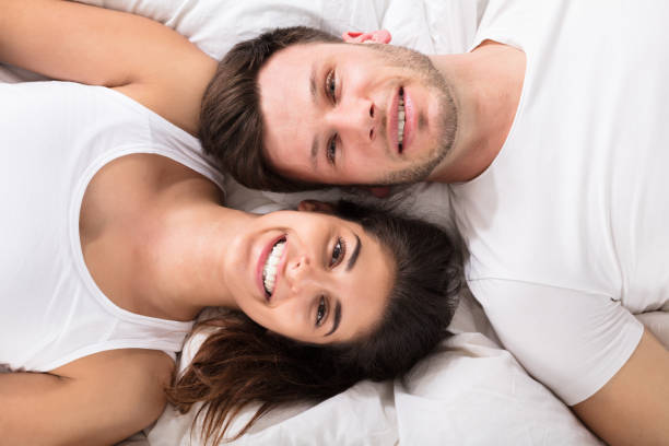 Elevated View Of Smiling Young Couple Lying On Bed